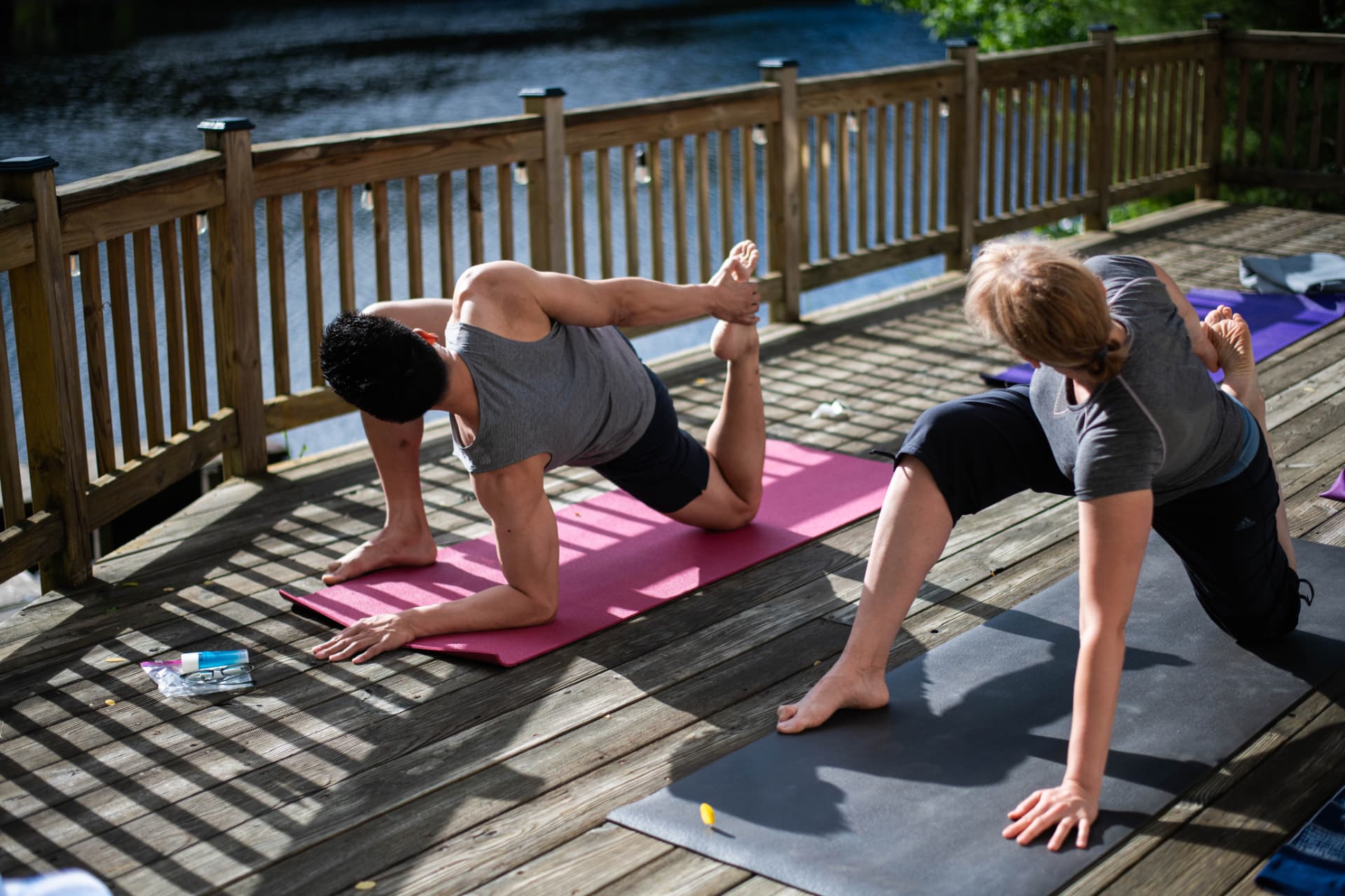 Two people doing yoga on a wooden deck beside the lake