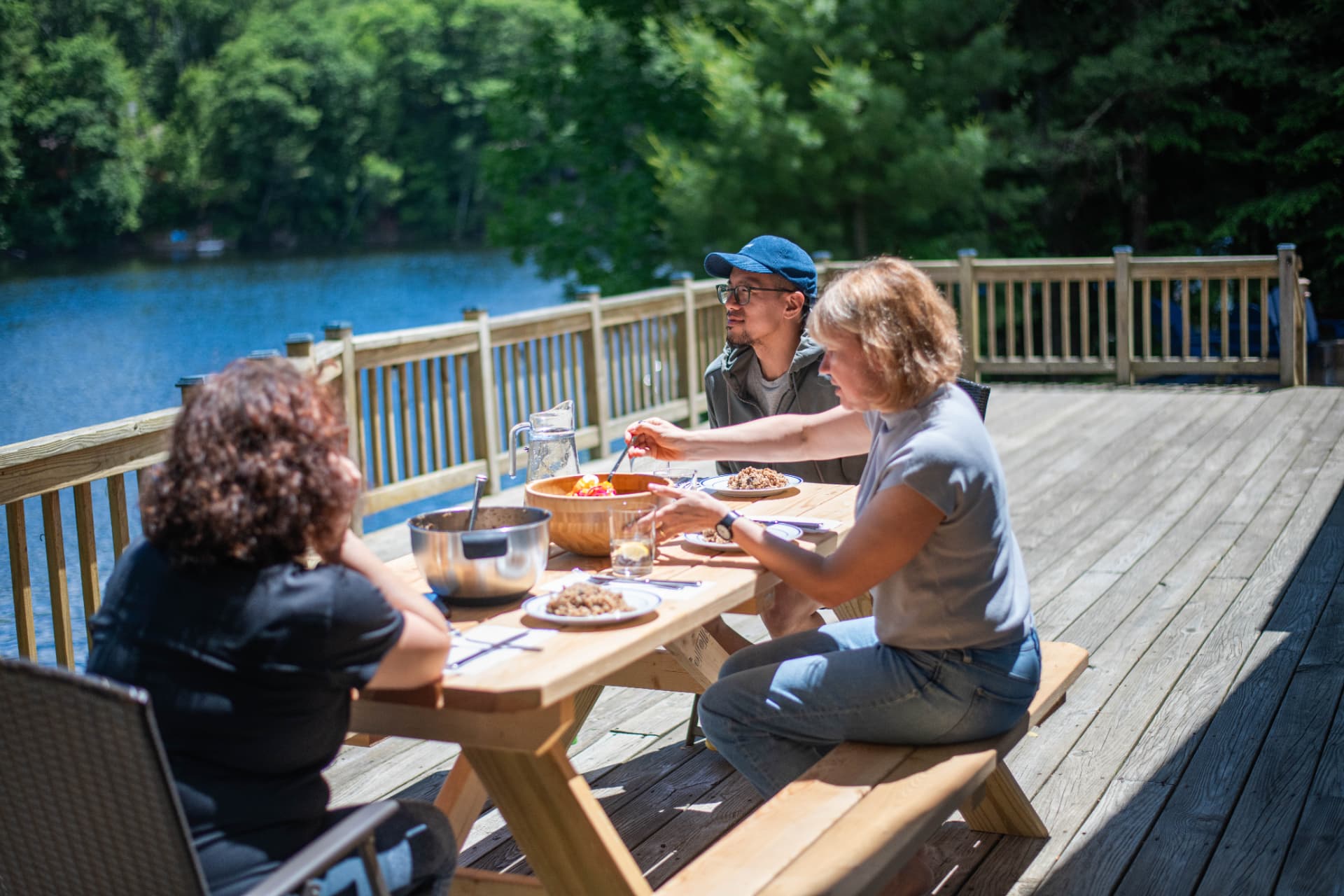 A group sharing a meal at a picnic table on the deck by the water
